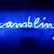 A bright blue neon sign spells out the word 'gambling' in cursive script. The background features a textured wall covered in domino tiles, also illuminated by the blue light, creating a vivid and visually striking scene.